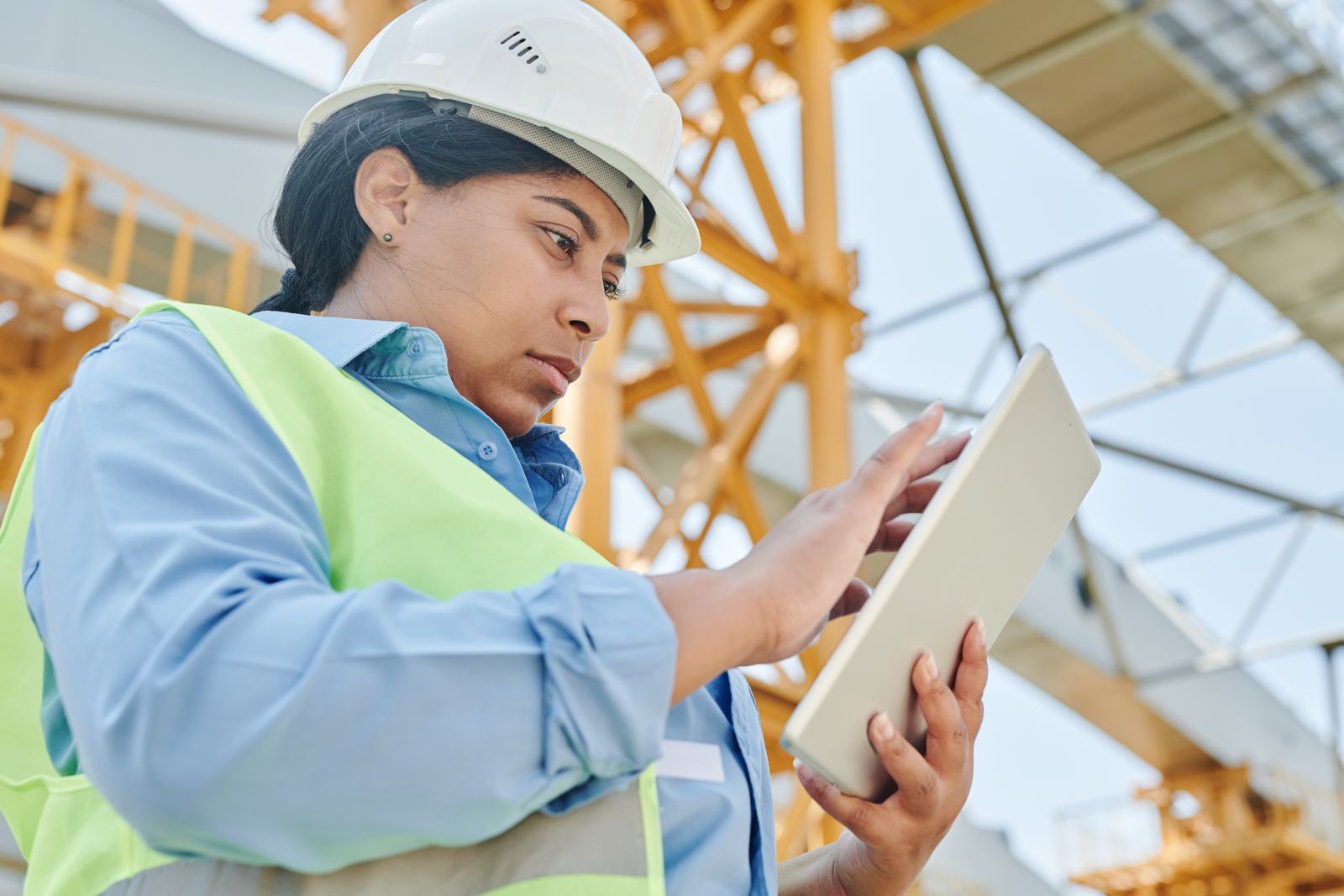 Field worker in a hard hat reviewing a tablet on a construction site